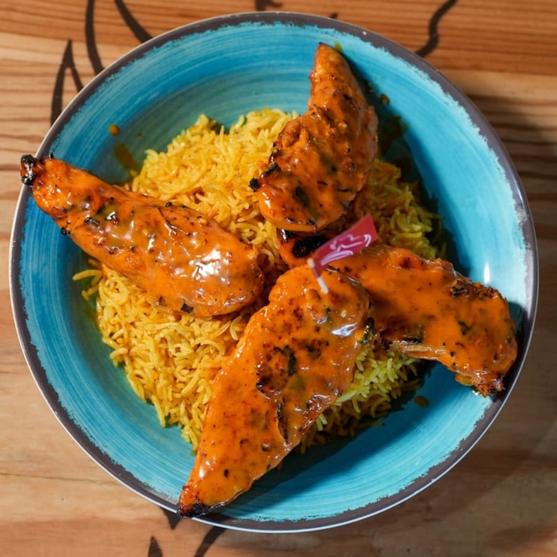Four peri-peri chicken tenders arranged on a bed of yellow rice in a blue bowl.