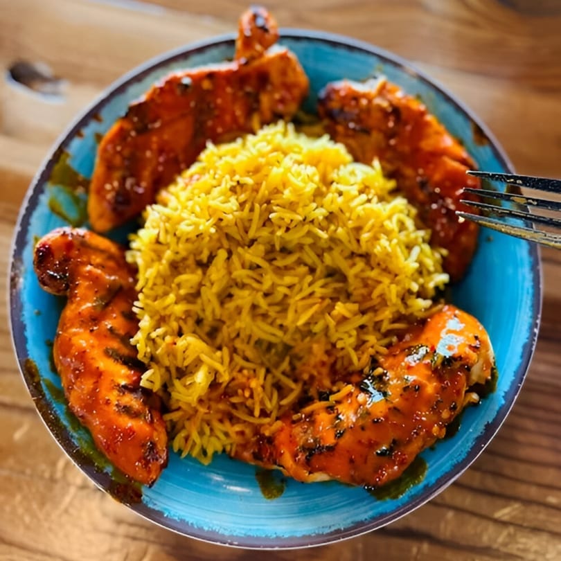 Peri-peri chicken tenders with yellow rice in a blue bowl on a wooden table.