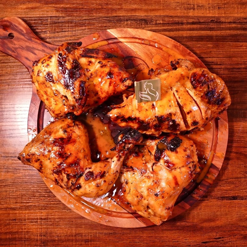Four pieces of grilled peri-peri chicken on a wooden serving board with a brand flag.