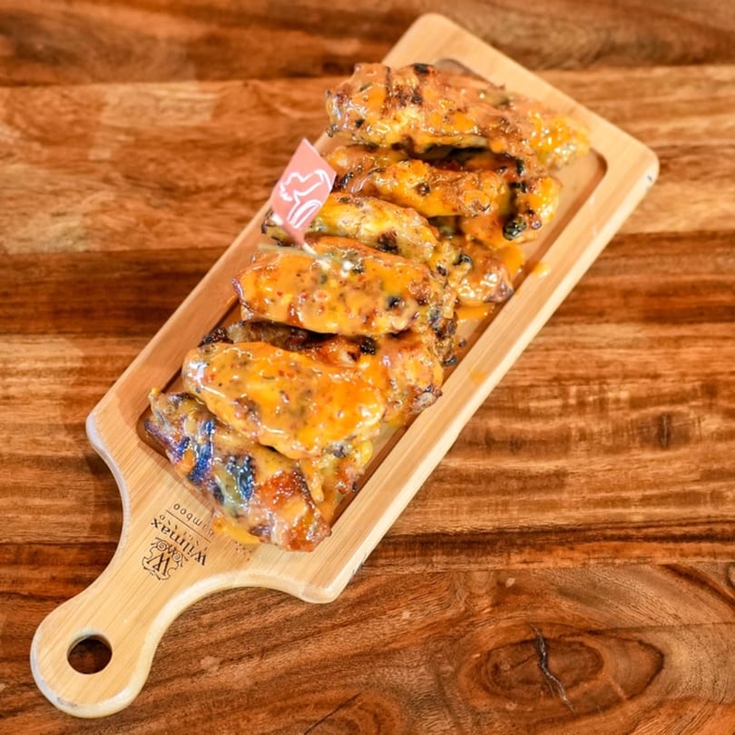 Peri-peri chicken wings with creamy orange sauce on a wooden serving board.