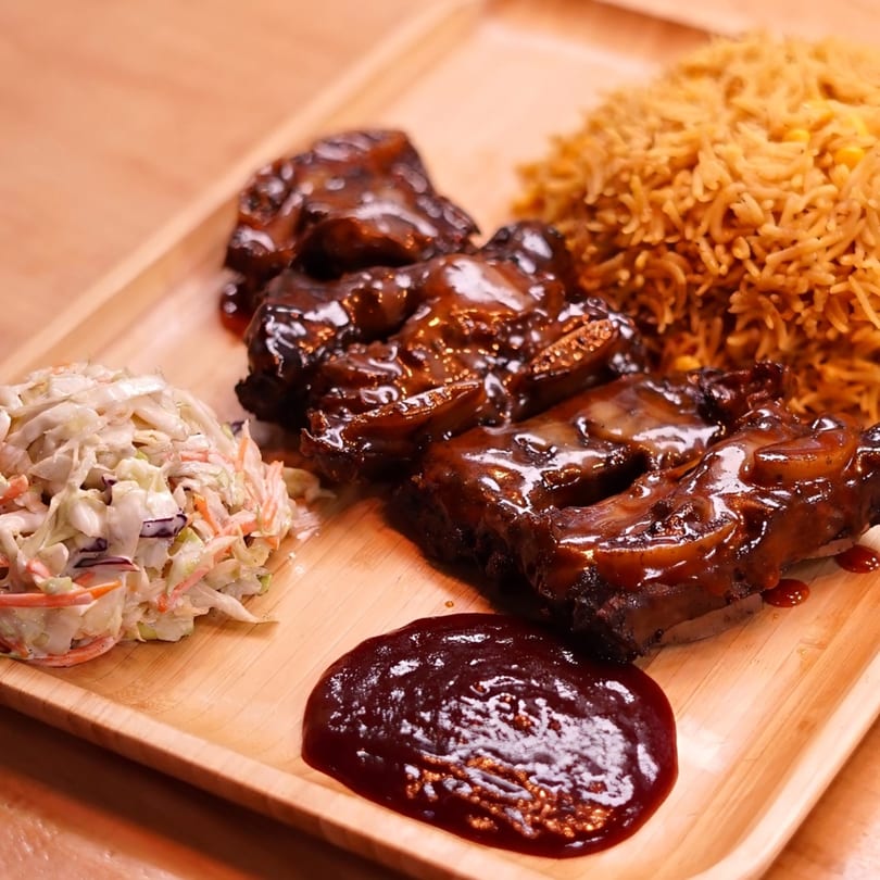 Peri-peri ribs with rice, coleslaw, and a side of sauce on a wooden tray.