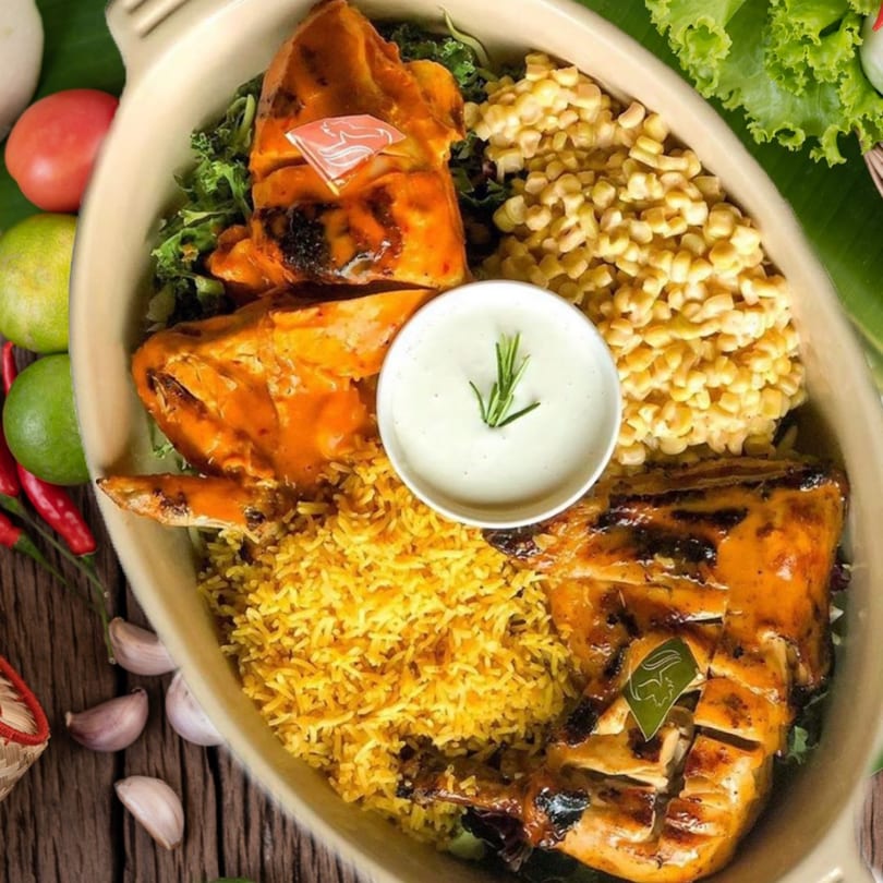 A Port of Peri Peri chicken platter with rice, corn, and a side of sauce.