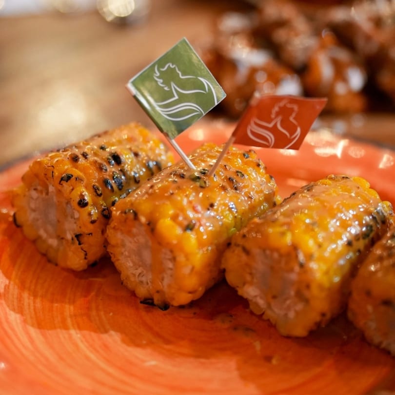 Grilled corn on the cob pieces, drizzled with sauce, and topped with Port of Peri Peri flags.