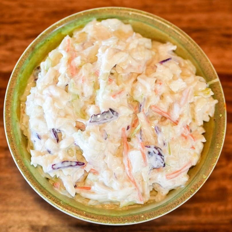 Creamy coleslaw with shredded cabbage, carrots, and red cabbage in a green bowl on a wooden table.