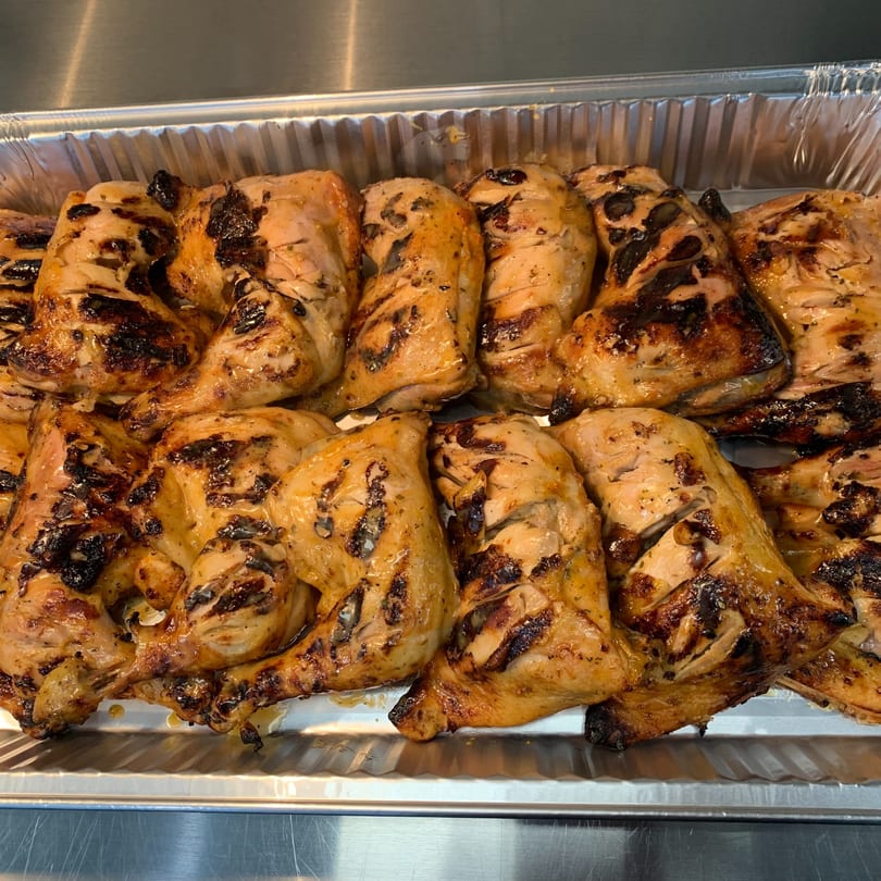 Grilled peri-peri chicken pieces with crispy, charred skin in a foil catering tray.