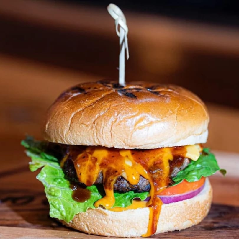 A juicy burger with melted cheese, lettuce, tomato, and red onion on a wooden surface.