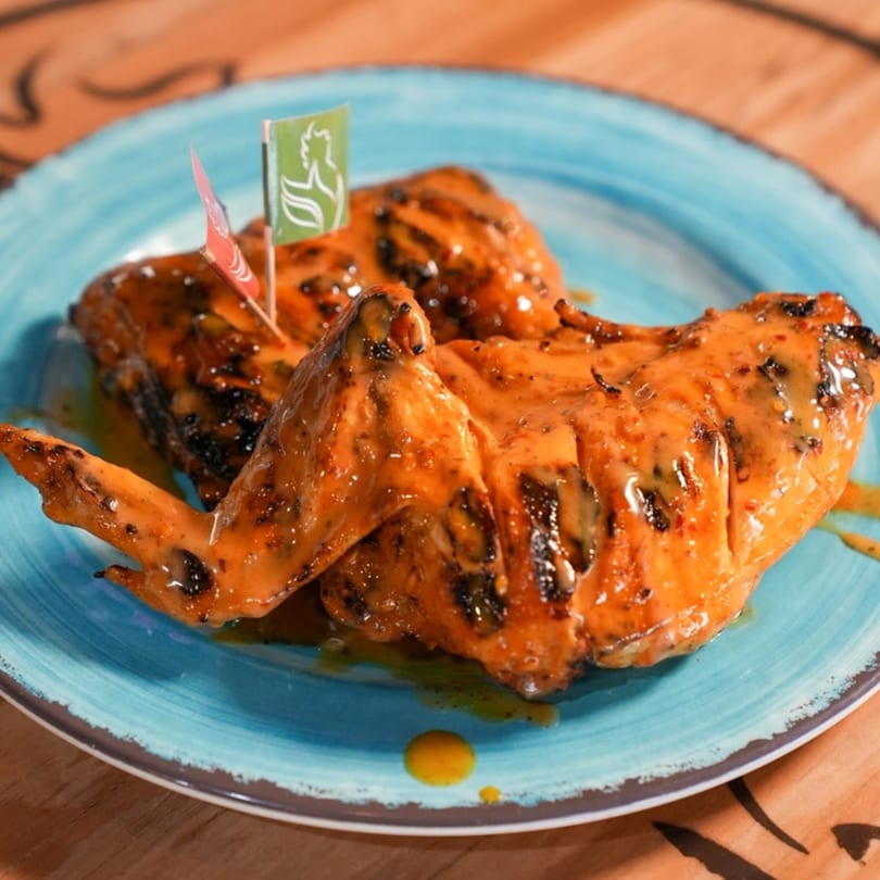 Two pieces of glazed peri-peri chicken with flags on a blue plate.