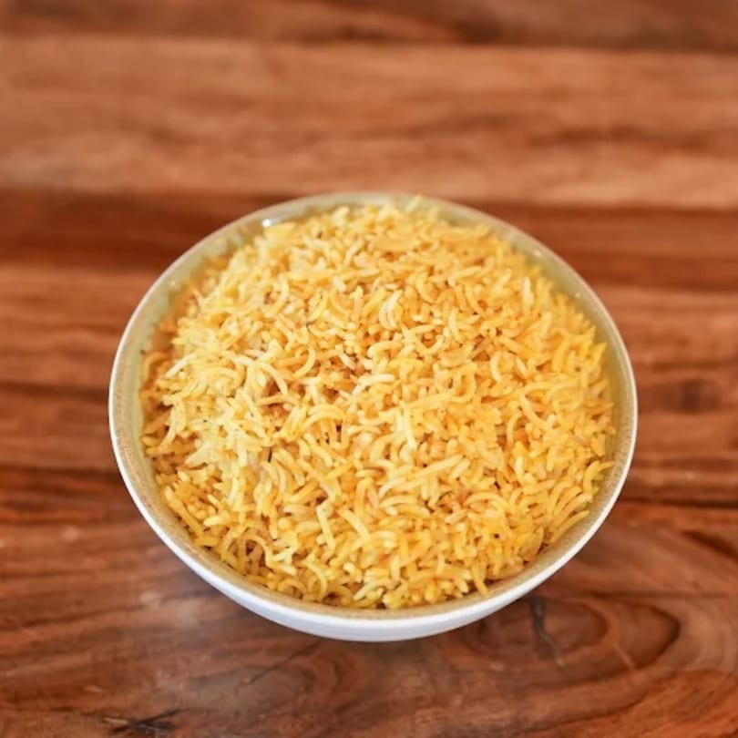 A white bowl filled with golden yellow rice sits on a rustic wooden table.