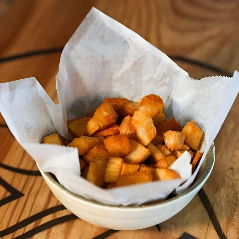 A white bowl filled with golden-brown, crispy peri-peri seasoned potato chunks, lined with white parchment paper.